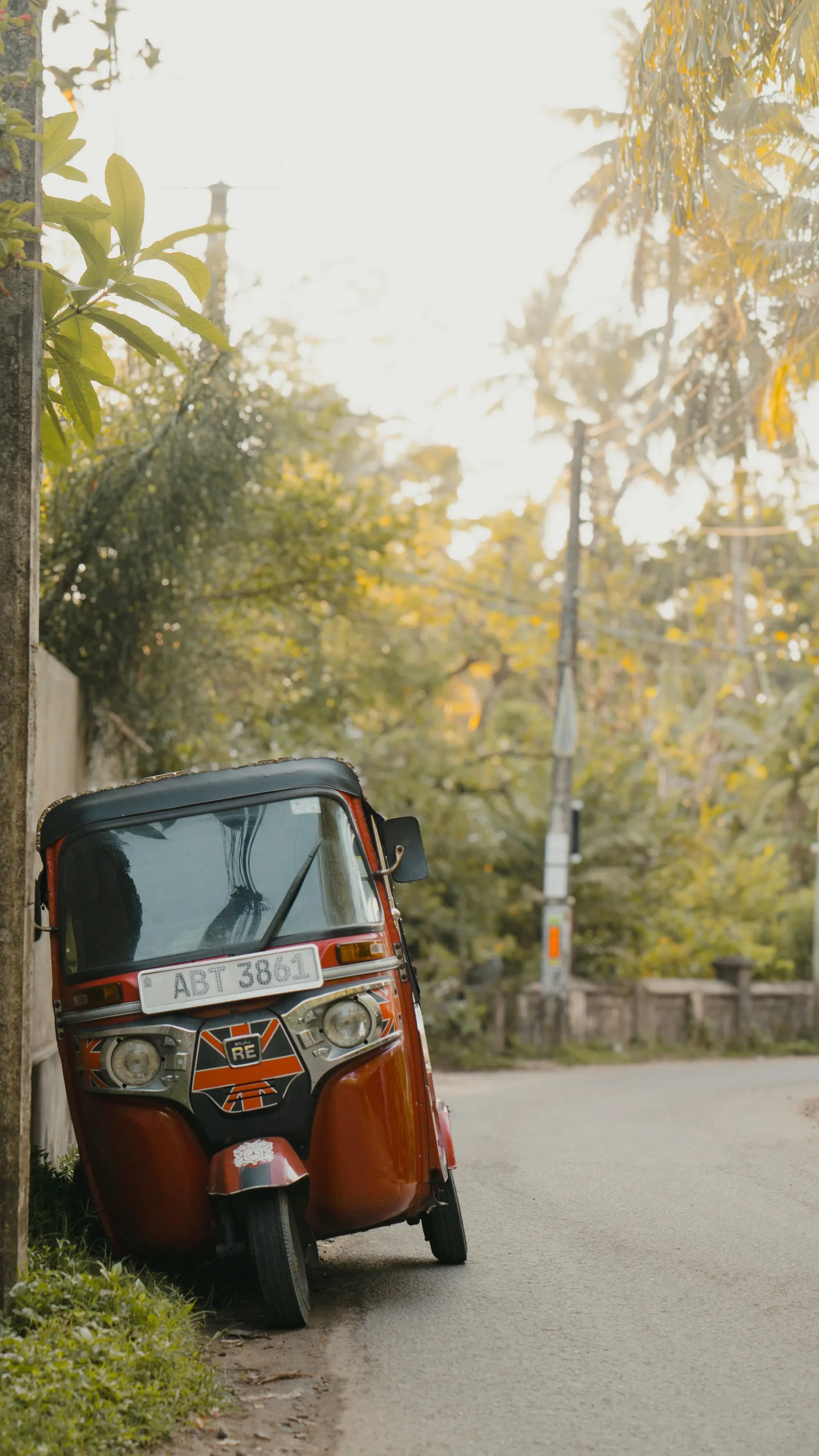 A red tuk-tuk on a tree-lined road in Sri Lanka